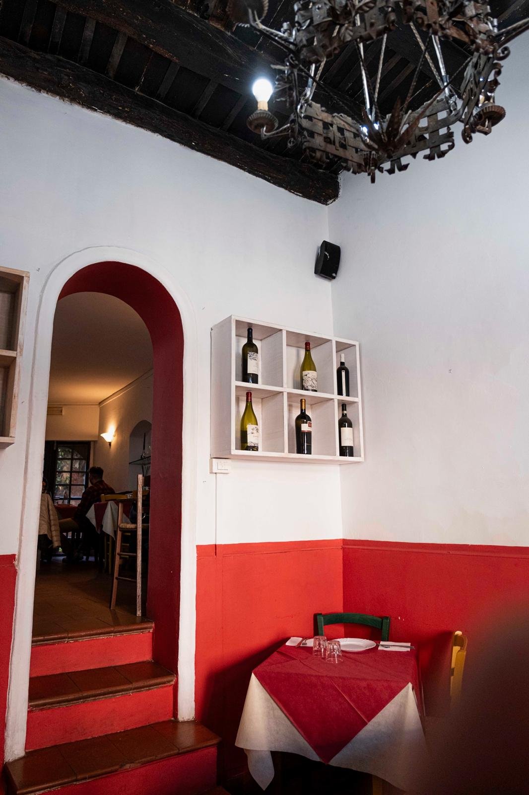 Sala dell'osteria con tavolo apparecchiato e bottiglie di vino